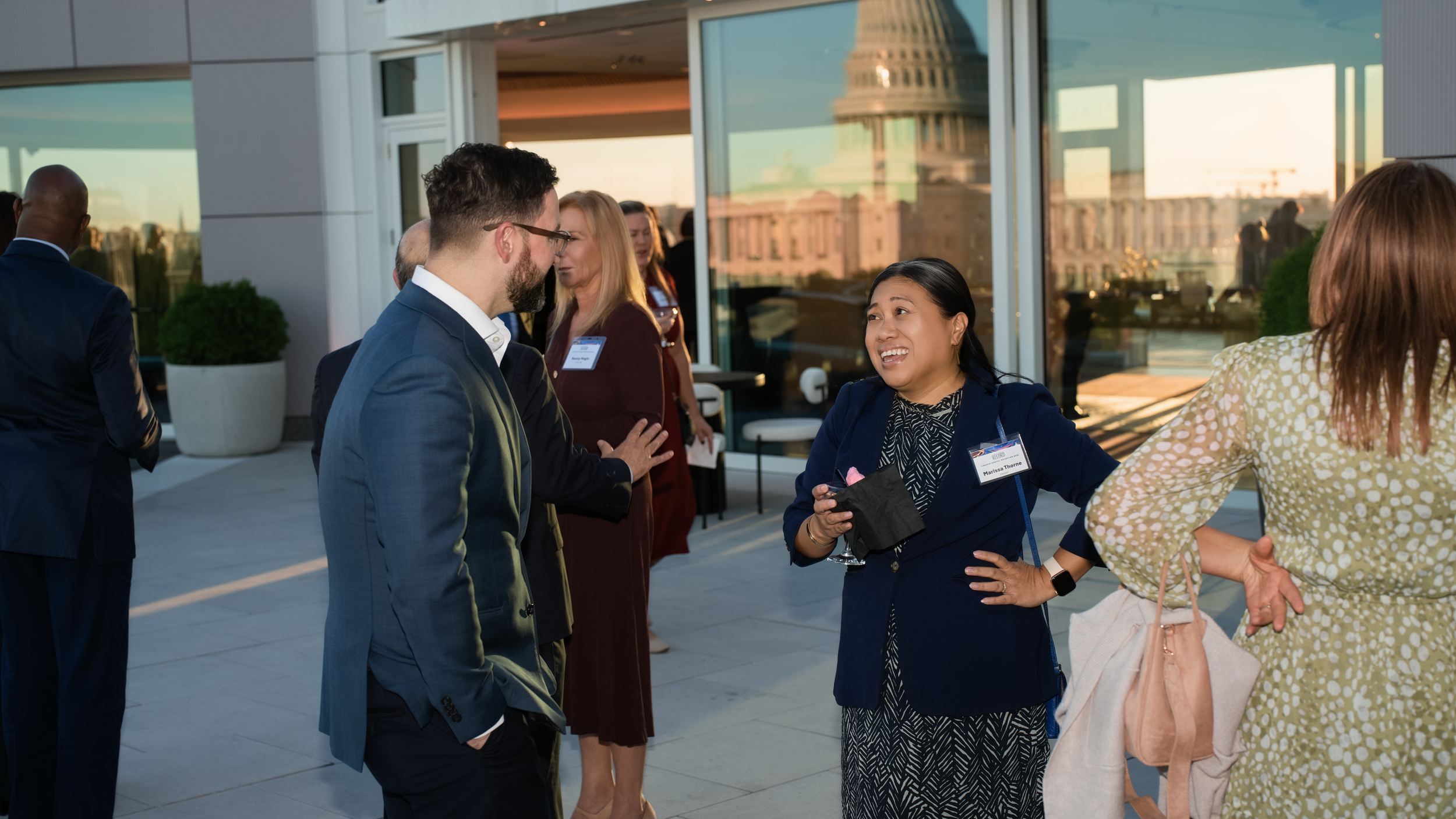 Guests converse on the 101 Constitution rooftop with the U.S. Capitol reflected in the glass behind them.
