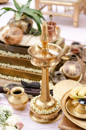 Brass Kerala nilavilakku lamp adorned with white flower garlands on a traditional wedding ceremony table with coconut and ritual vessels.