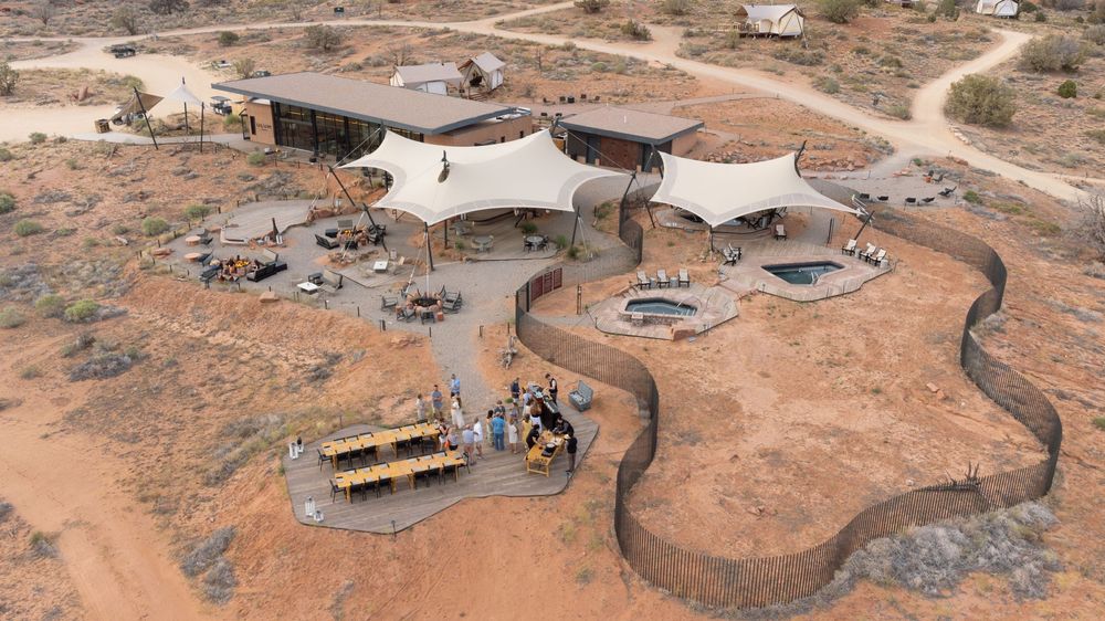 Aerial view of a luxury desert lodge with white tent structures, outdoor seating, and a curved pathway in an arid landscape.