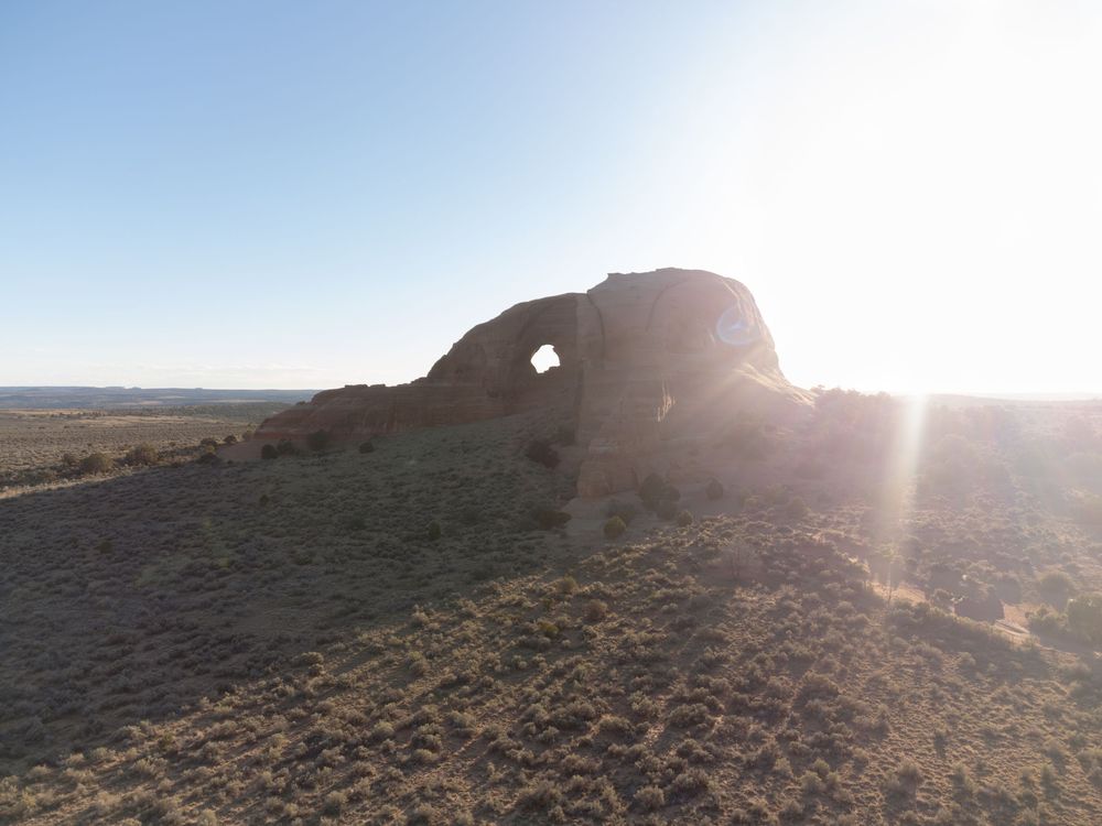 Sun-lit ancient rock arch formation rising from arid desert plains under a clear blue sky.