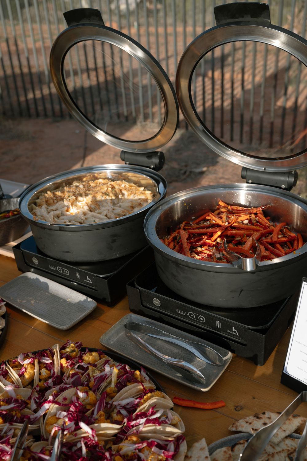 Two open electric buffet warmers with rice and spiced carrots beside fresh radicchio salad on a wooden table.