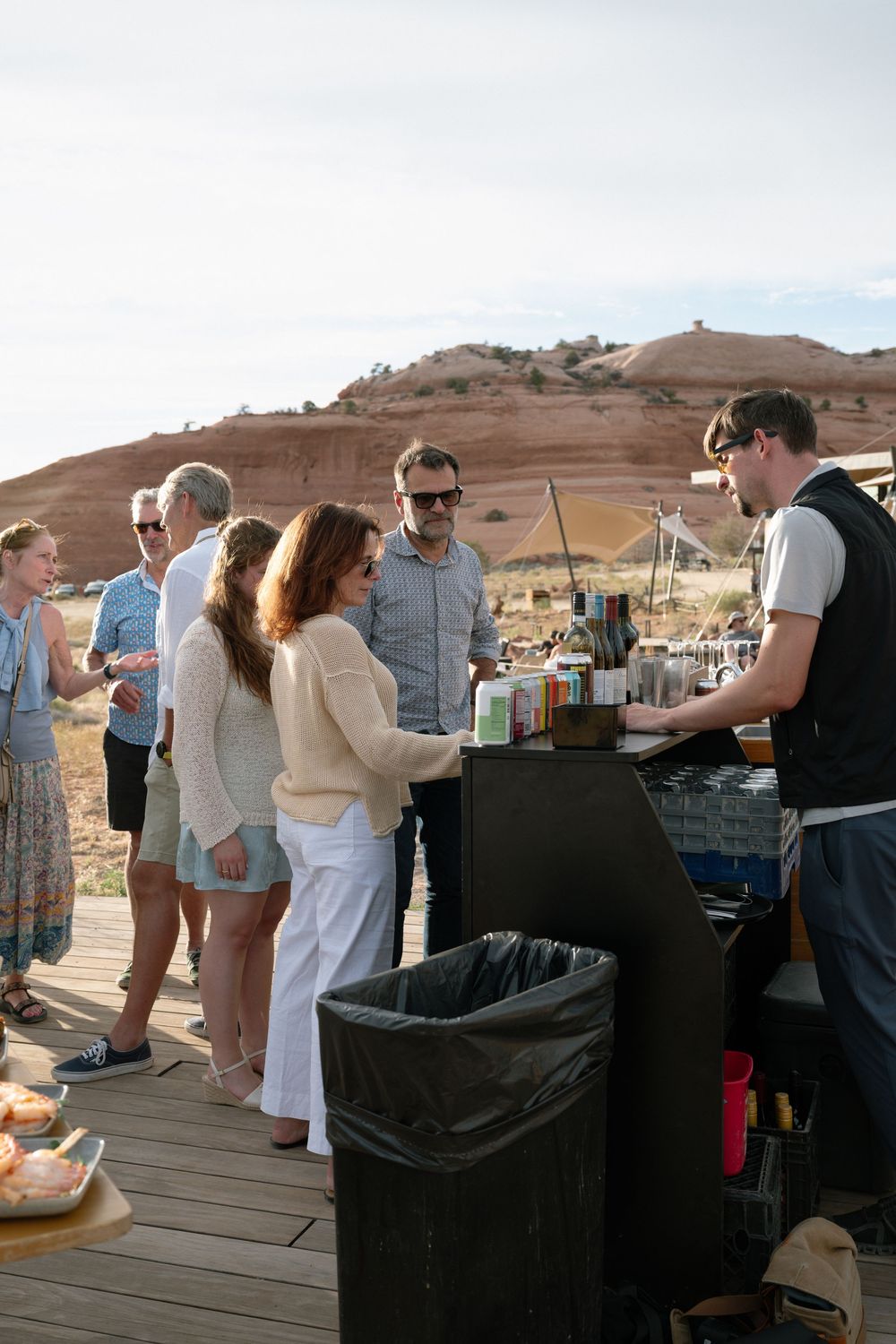 Guests gather at an outdoor bar setup on a wooden deck with red rock desert landscape in the background.