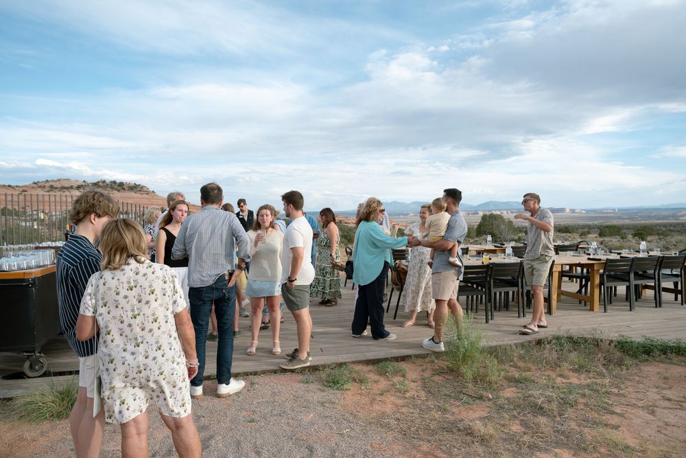 Guests mingle on an outdoor terrace with scenic desert landscape views during a casual social gathering.