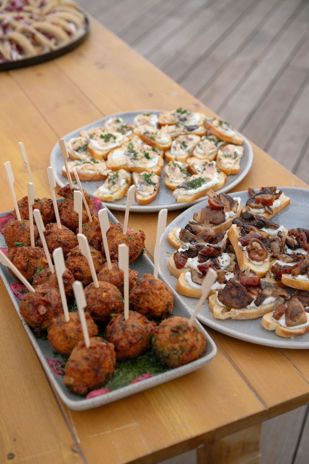 Appetizer spread featuring meatballs on sticks, bruschetta, and topped crostini on a wooden table.