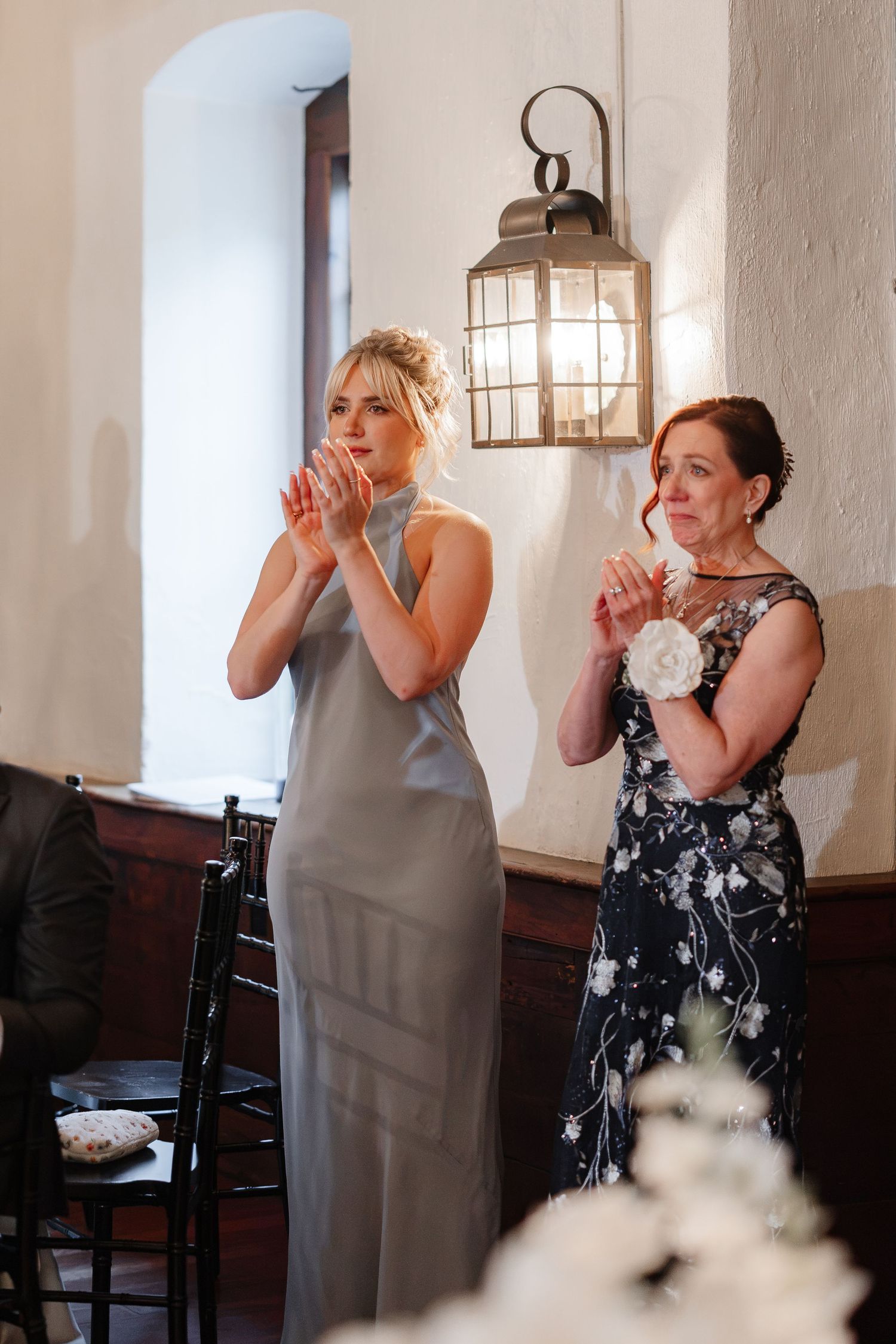 Bridesmaid in silver gown and mother of bride applaud during wedding reception.