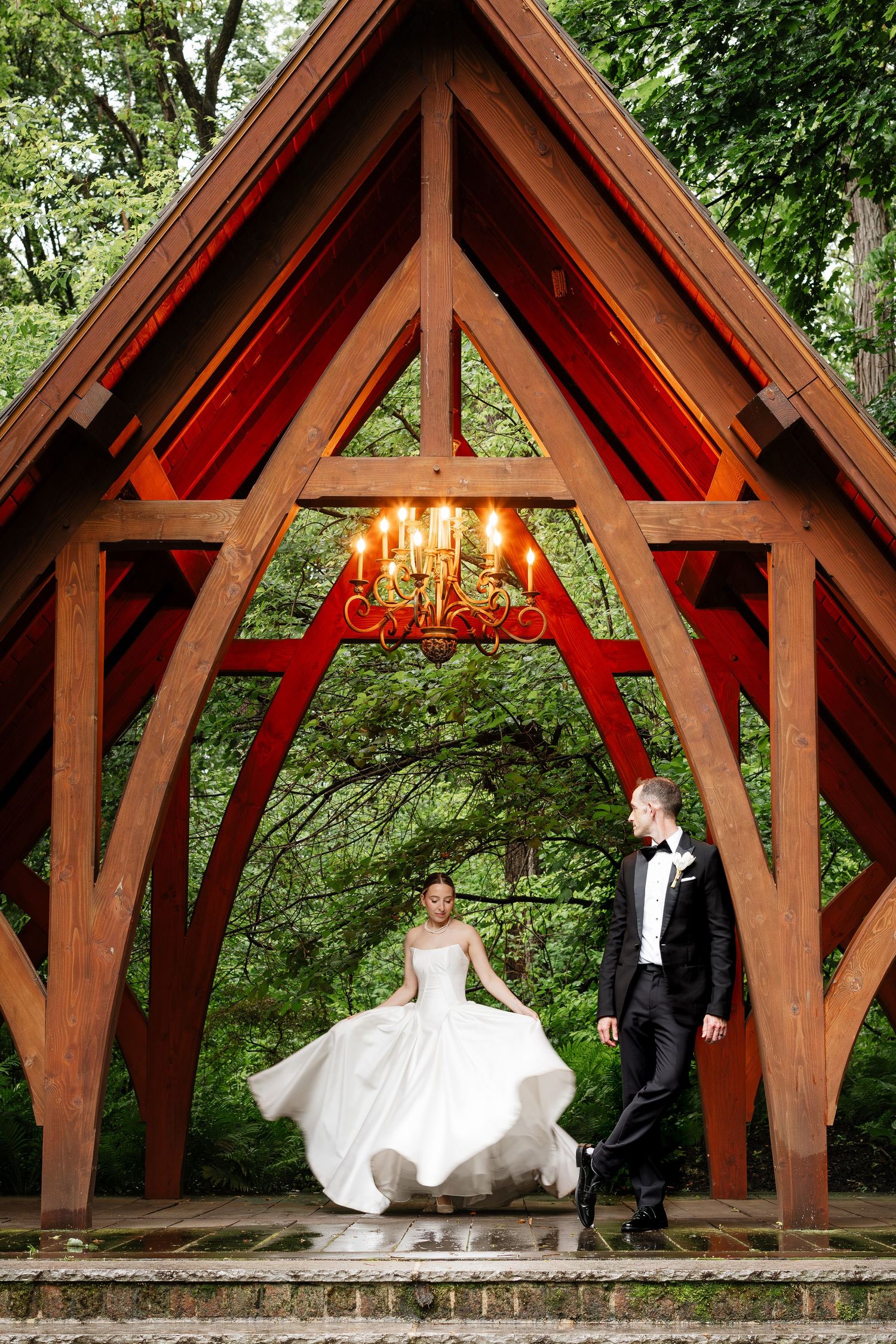 Bride twirling white ball gown under stunning red wooden arch with chandelier at wedding.