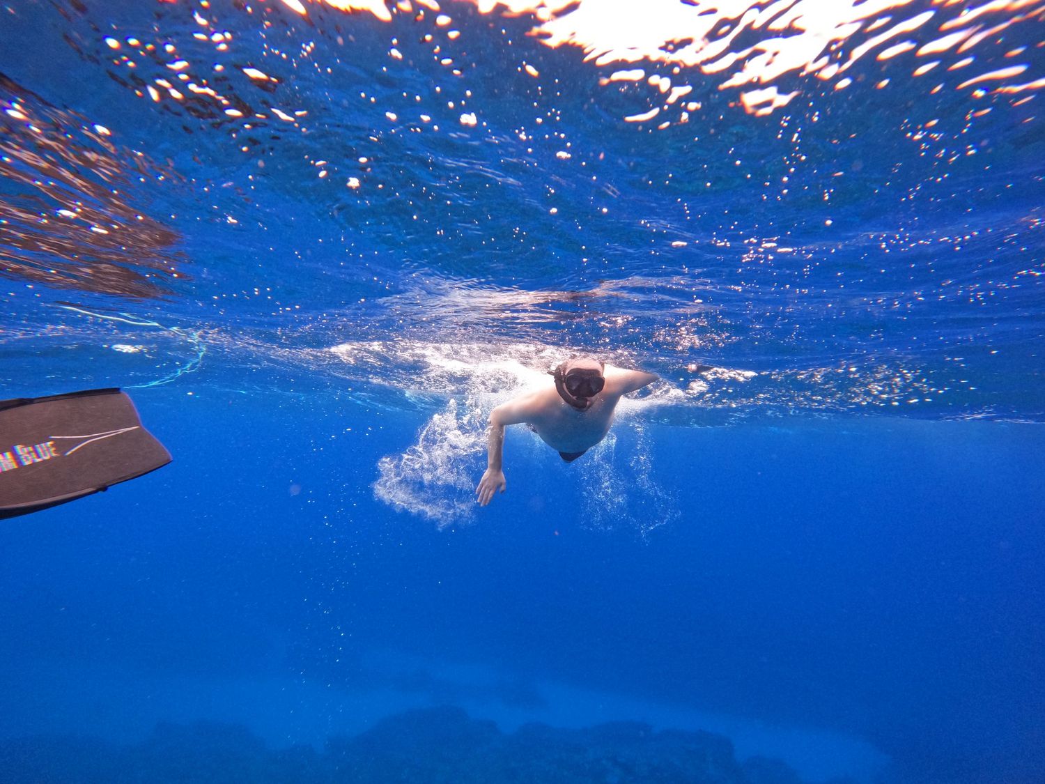 Underwater view of swimmer gliding through crystal blue ocean waters.