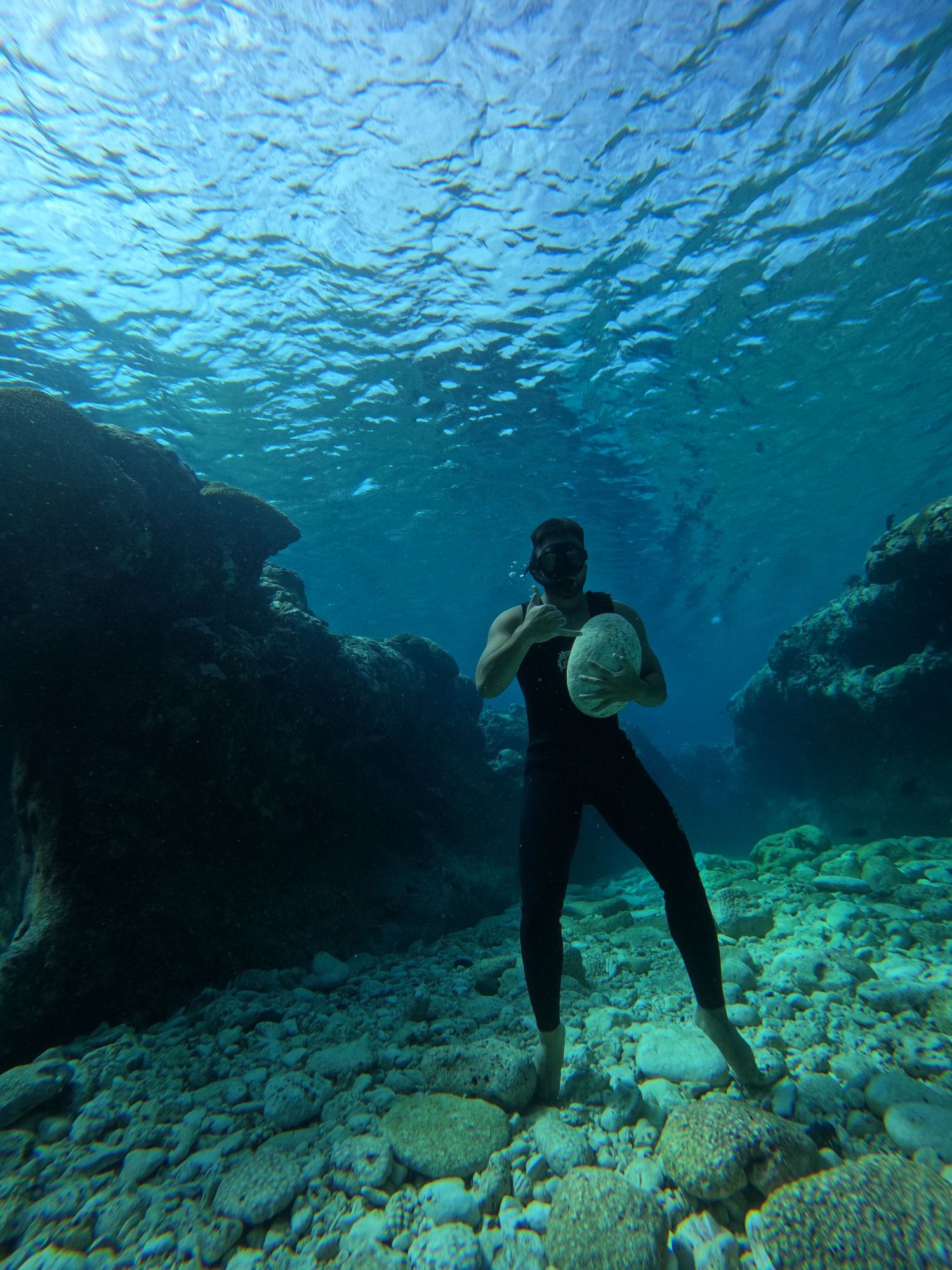 Snorkeler stands on ocean floor near rocky underwater formations in turquoise waters.