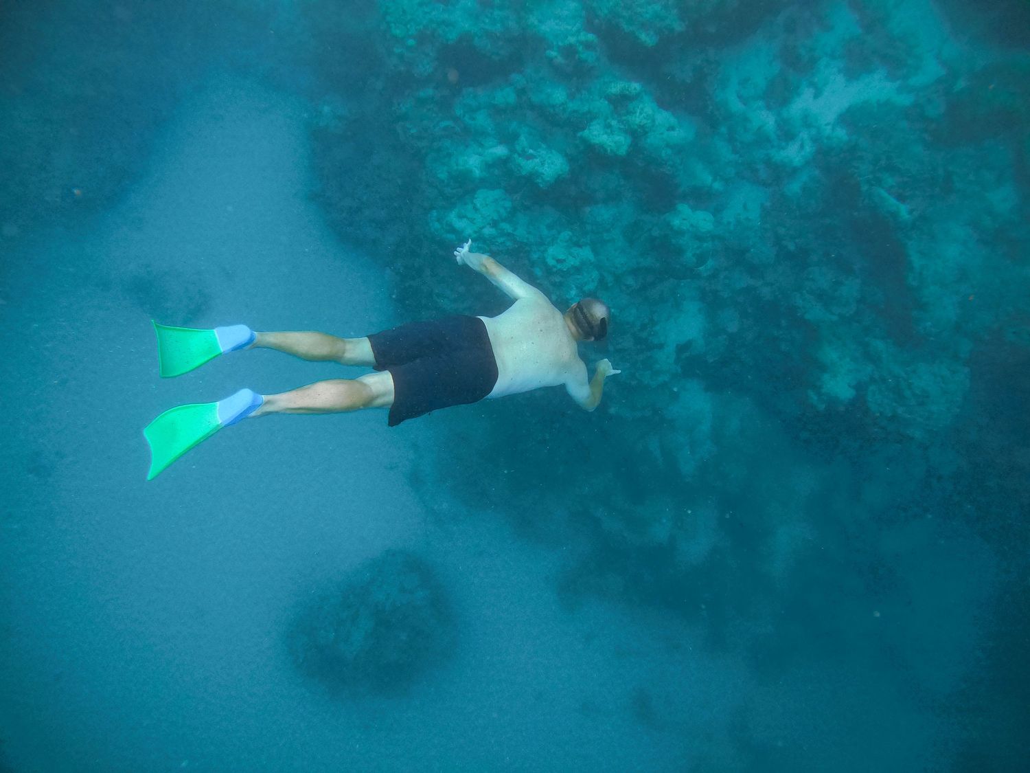 Snorkeler with blue fins explores underwater reef formations in turquoise waters.