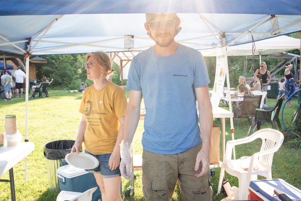 Two people standing under a canopy tent at an outdoor community event on a sunny day.