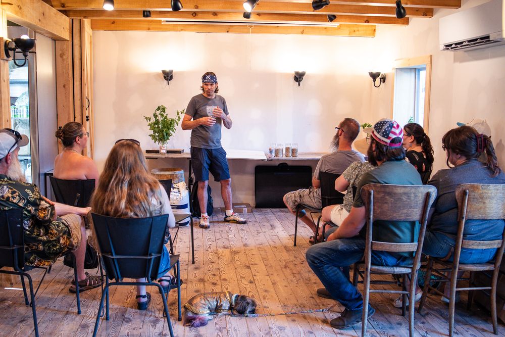 A man presenting to a small group seated in chairs inside a rustic wooden room.