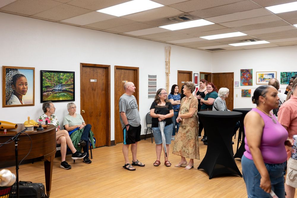 People mingling at an art gallery opening with colorful paintings displayed on white walls in a bright community space.