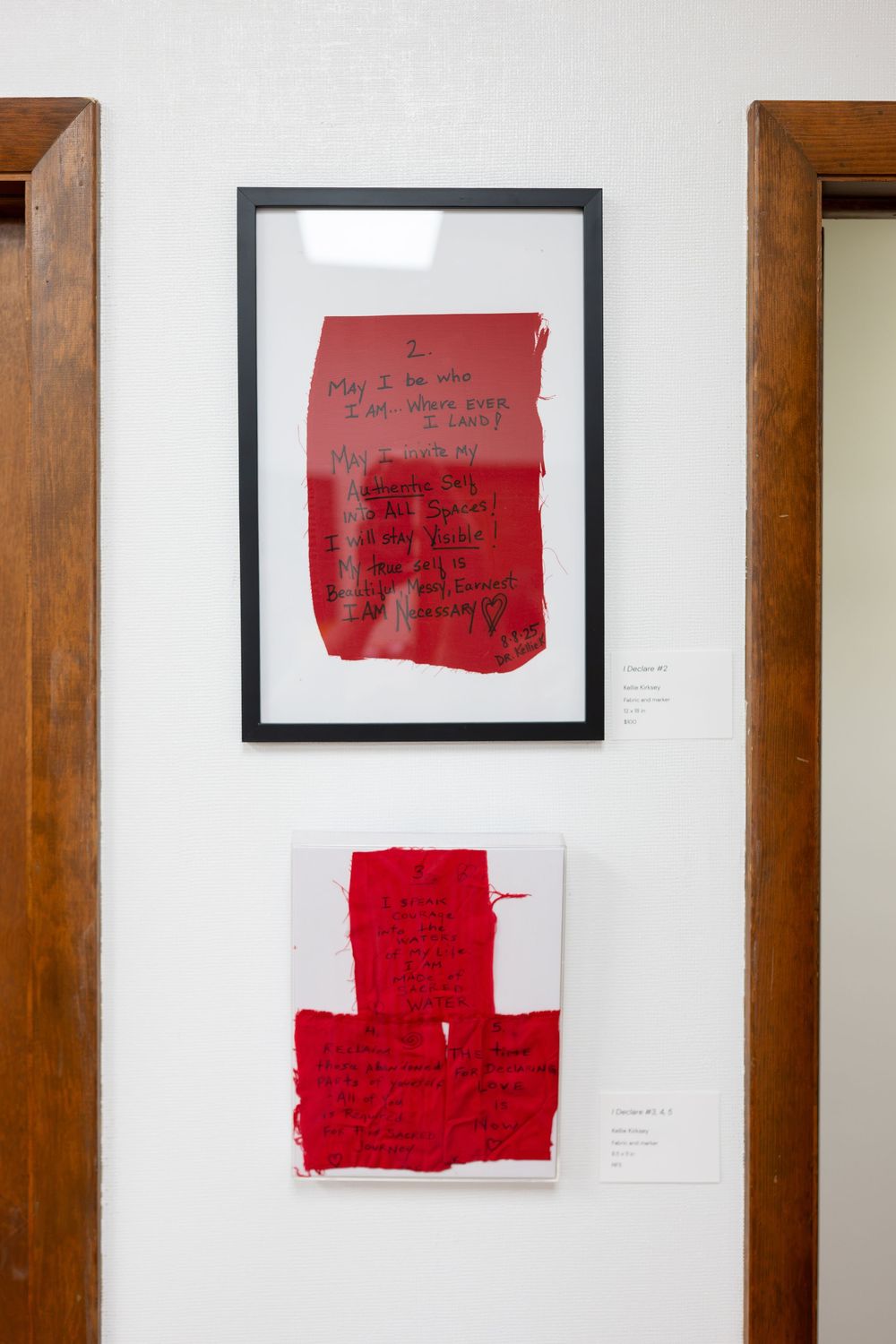 Framed red abstract artwork with handwritten text displayed on a white gallery wall.