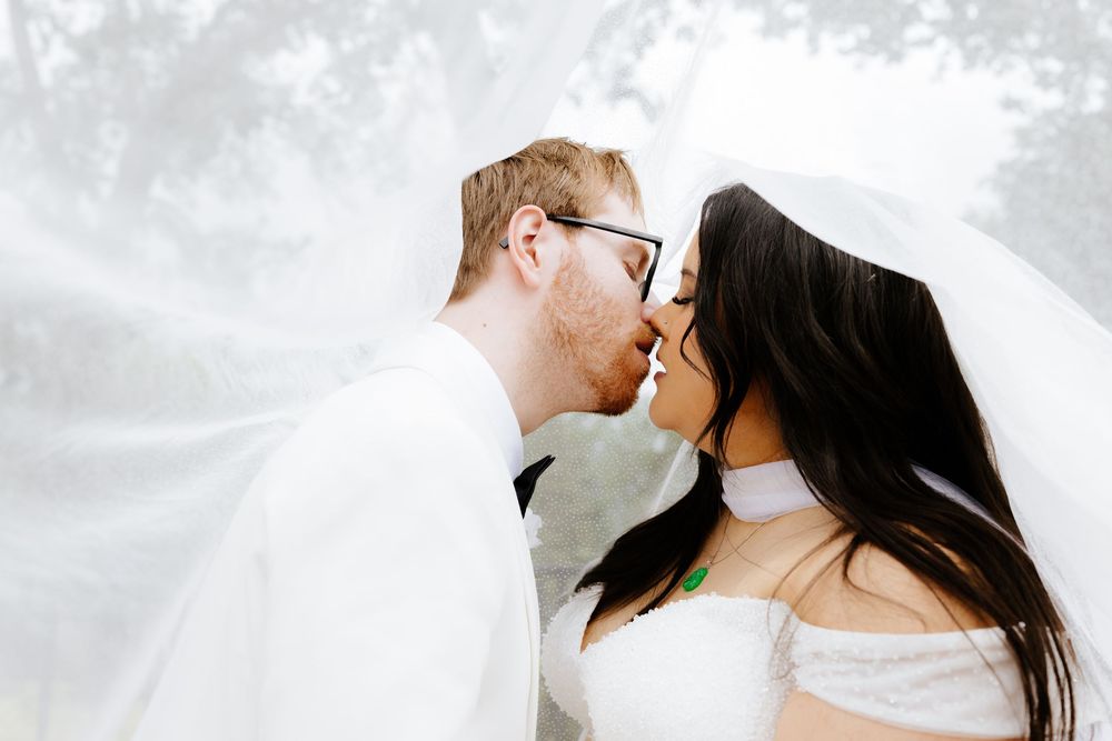 A newlywed couple shares a romantic kiss under a flowing white veil on their wedding day.