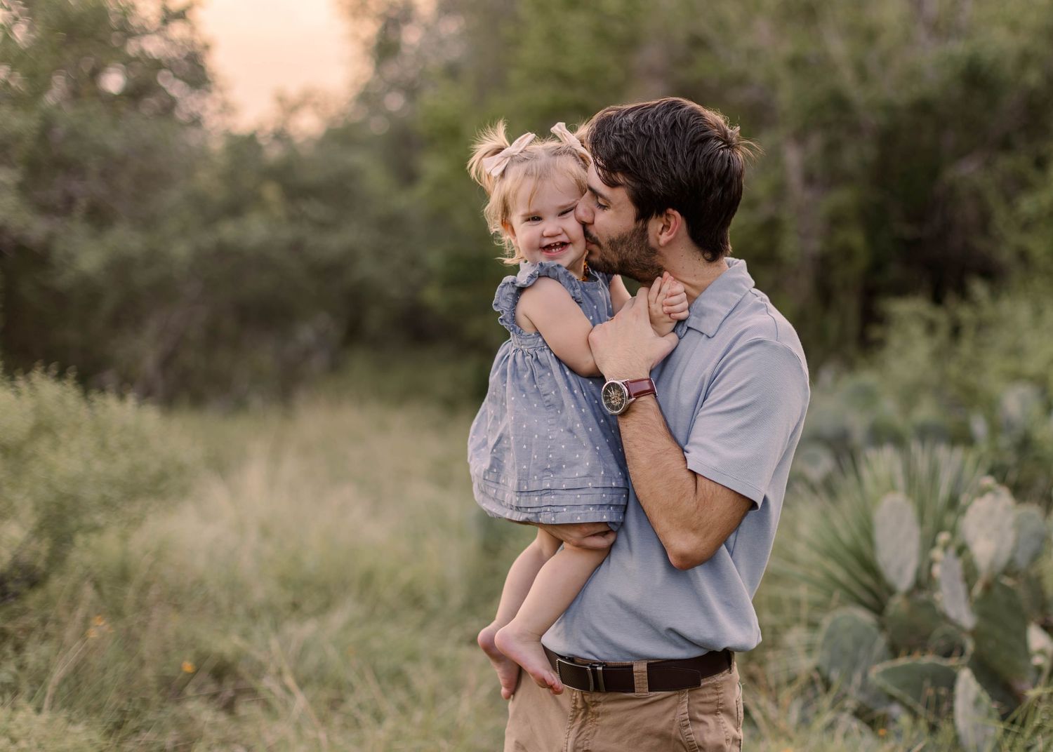 A smiling boy stands between his pregnant mother and father outdoors in a warm family maternity portrait session.