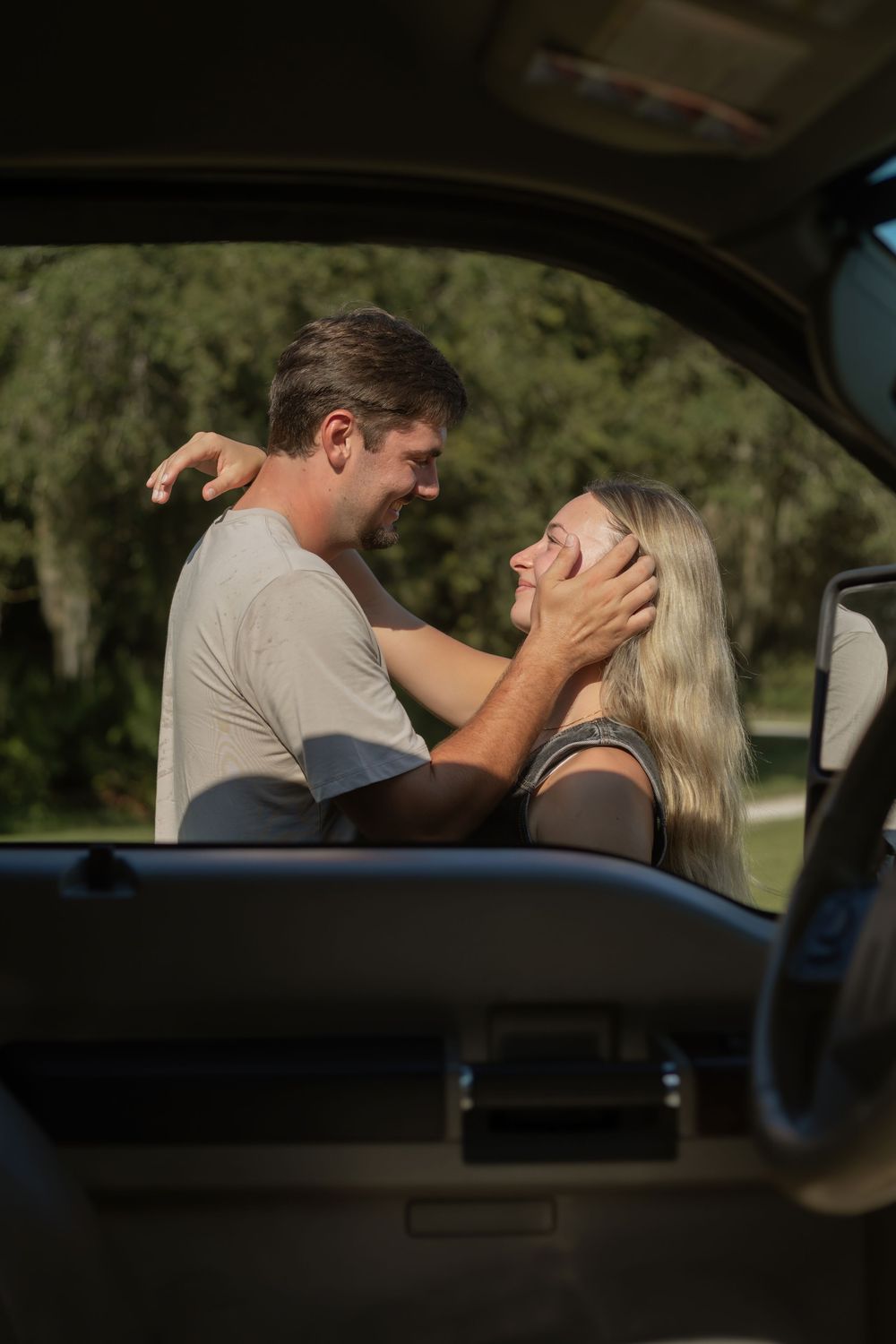Loving couple sharing a tender moment by a car, man gently holding woman's face while smiling at each other.