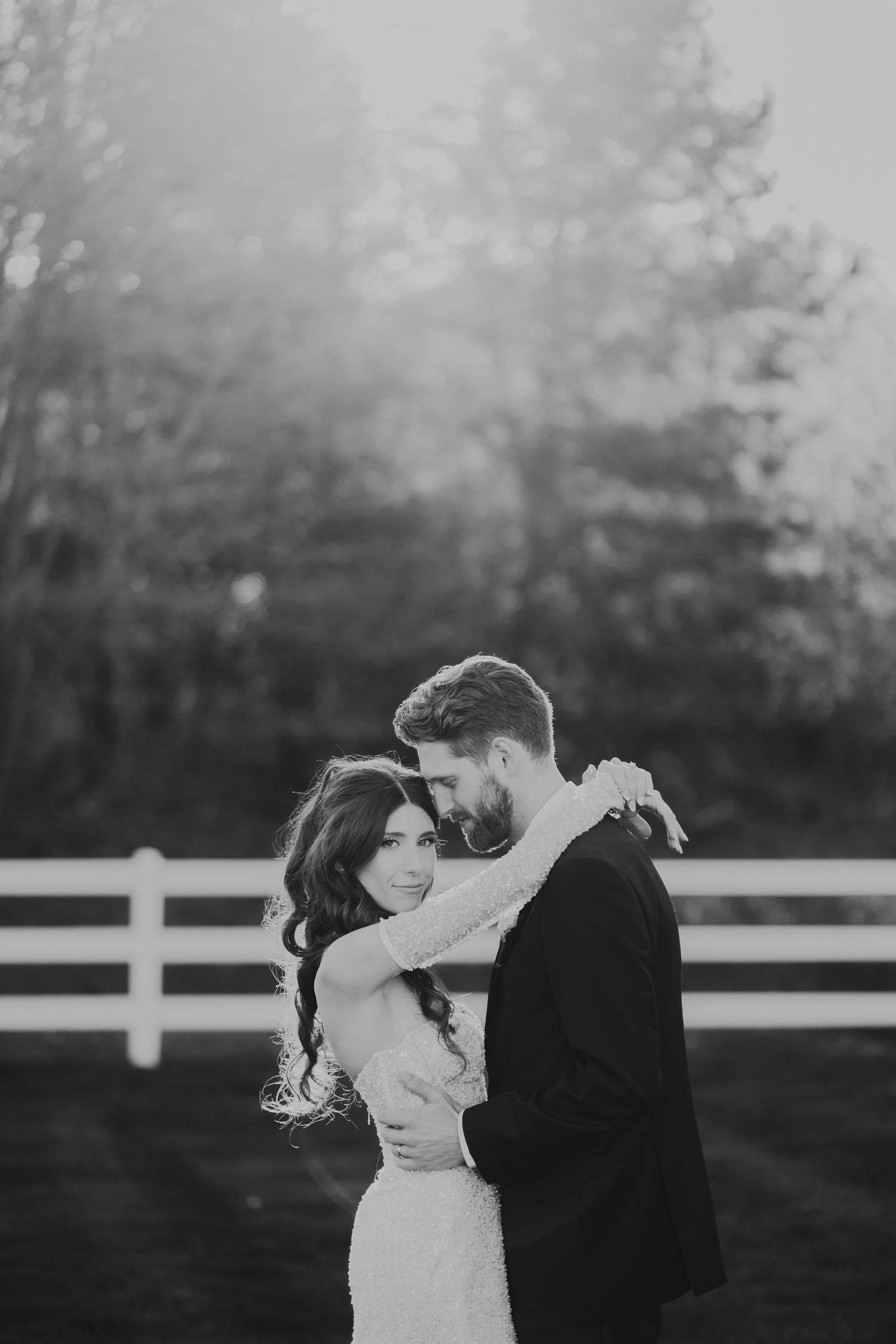 Black and white photo of a couple embracing outdoors near a white fence, sharing a romantic moment at venue bella giornata.