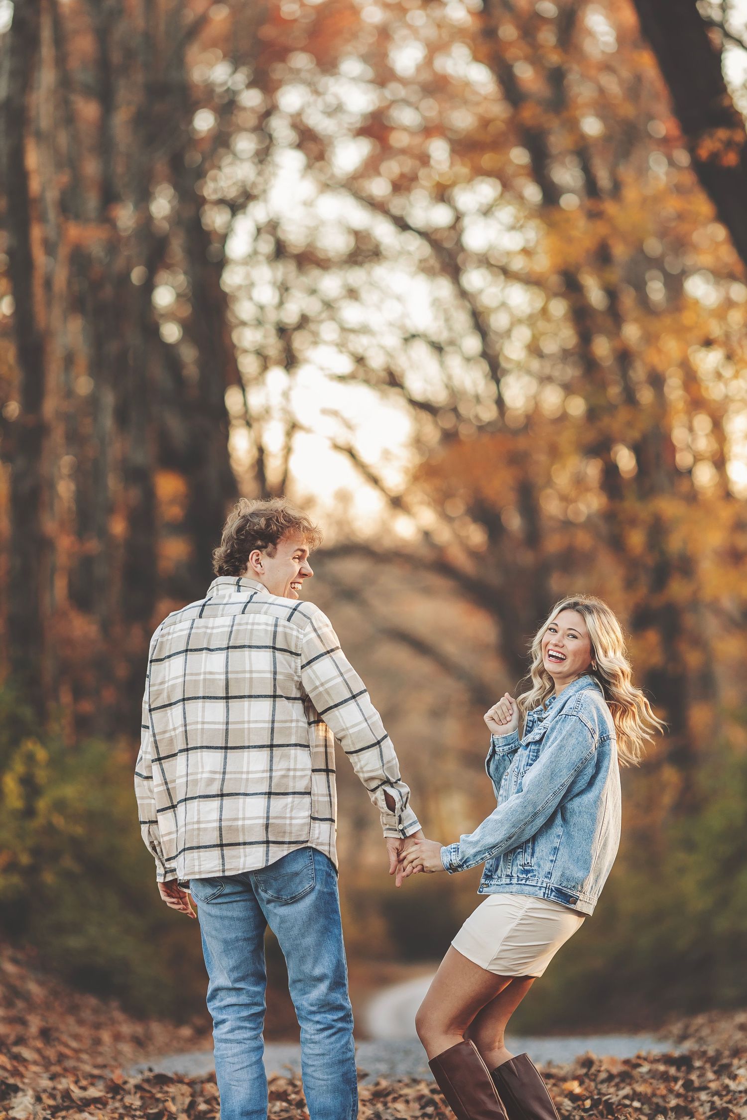 Couple embracing outdoors in autumn light, woman smiling with engagement ring visible, warm bokeh background.