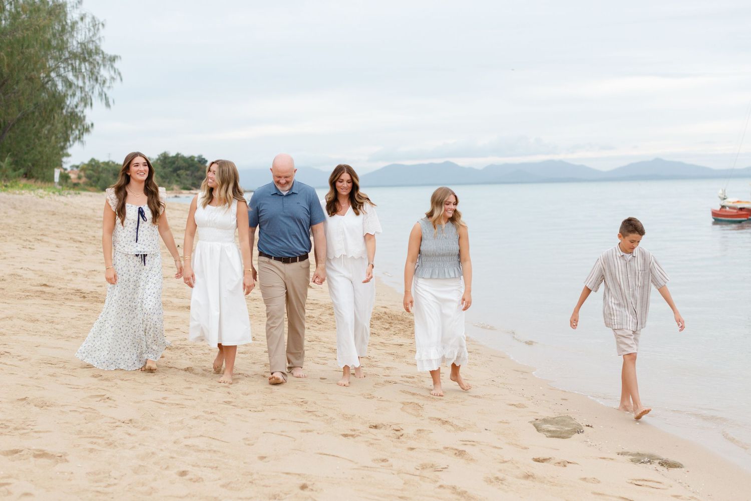Family of six smiling together on a beach with mountains in the background on a cloudy day.