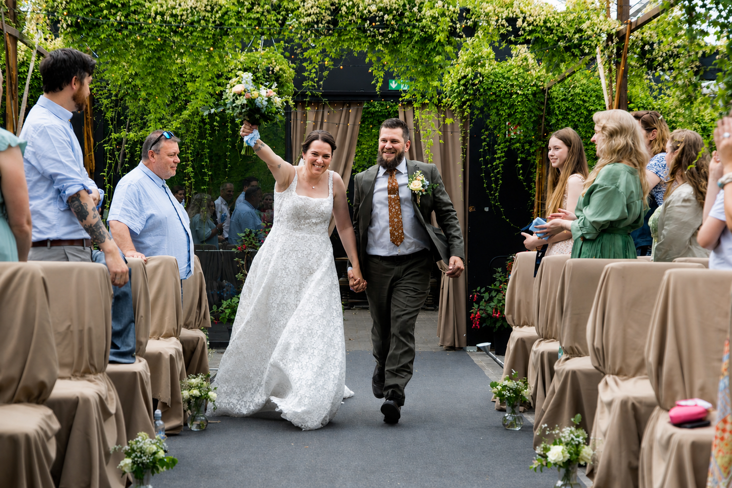 Happy newlyweds walk down the aisle after their outdoor wedding ceremony surrounded by lush greenery.