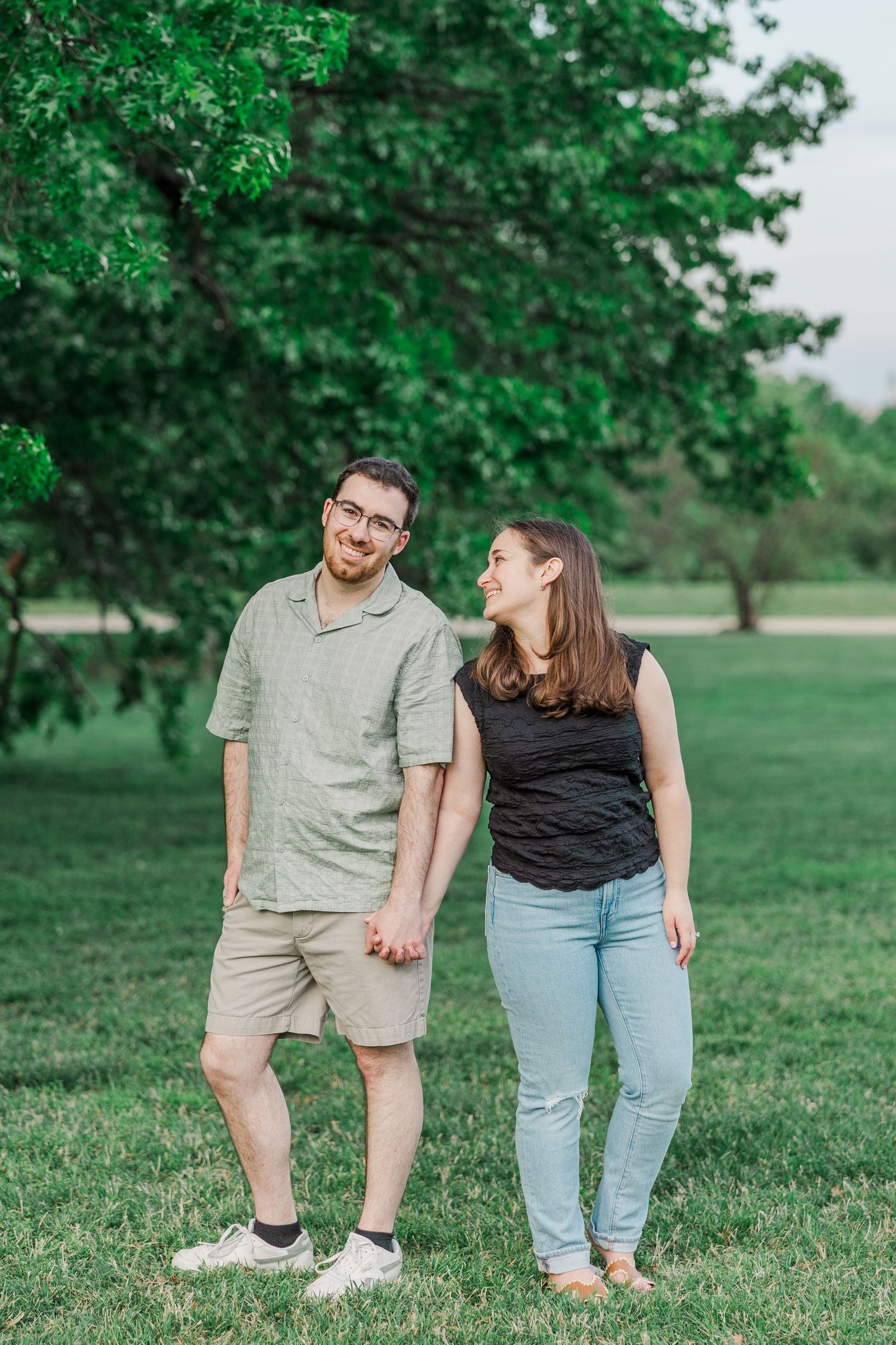 Couple embracing in a garden surrounded by blooming tulips and lush green trees during a romantic outdoor engagement session.