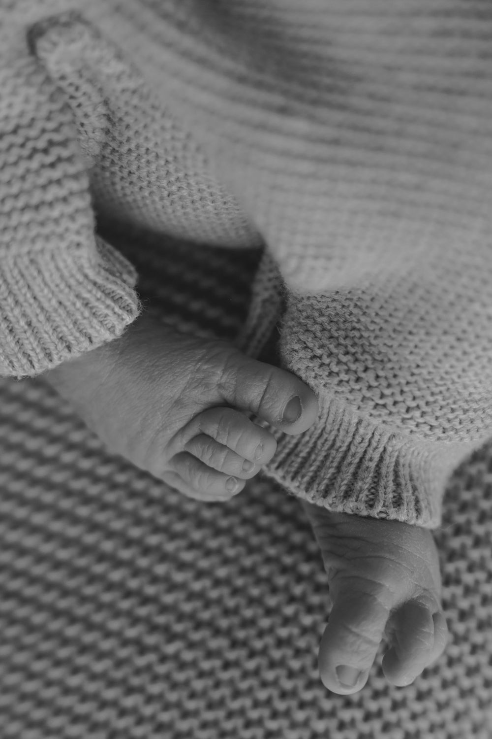 Black and white close-up photo of a newborn baby's tiny feet and toes in a knit sweater.