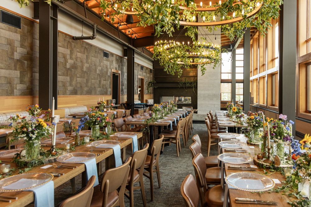 Elegant wedding reception venue with wooden tables, wildflower centerpieces, and lush greenery chandeliers in a rustic modern space.