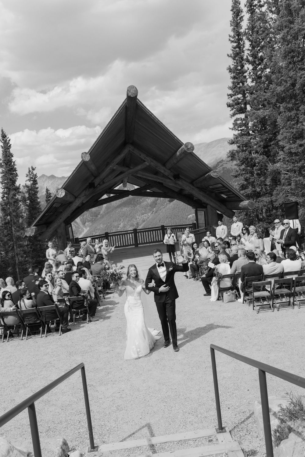 Black and white photo of newlyweds walking down the aisle at an outdoor mountain wedding ceremony in Banff.
