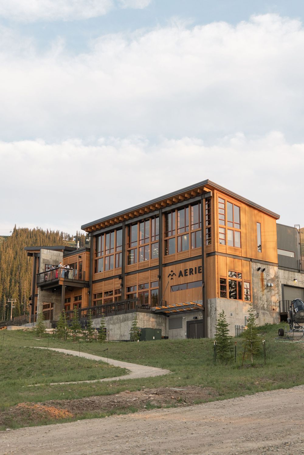 Two-story wooden Aerie building with large windows and concrete base, set against a partly cloudy sky.