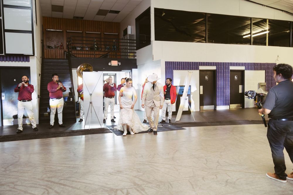 Group of performers in white and maroon outfits rehearsing in a large indoor venue with onlookers watching.