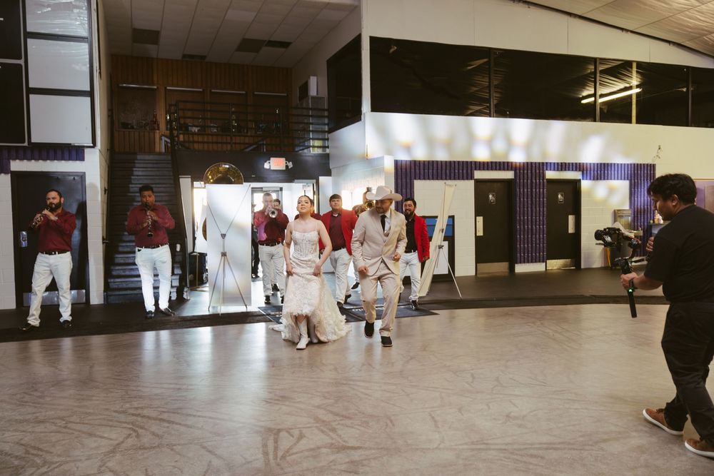 Wedding party walks through venue entrance in formal attire including white gown and cowboy hats.