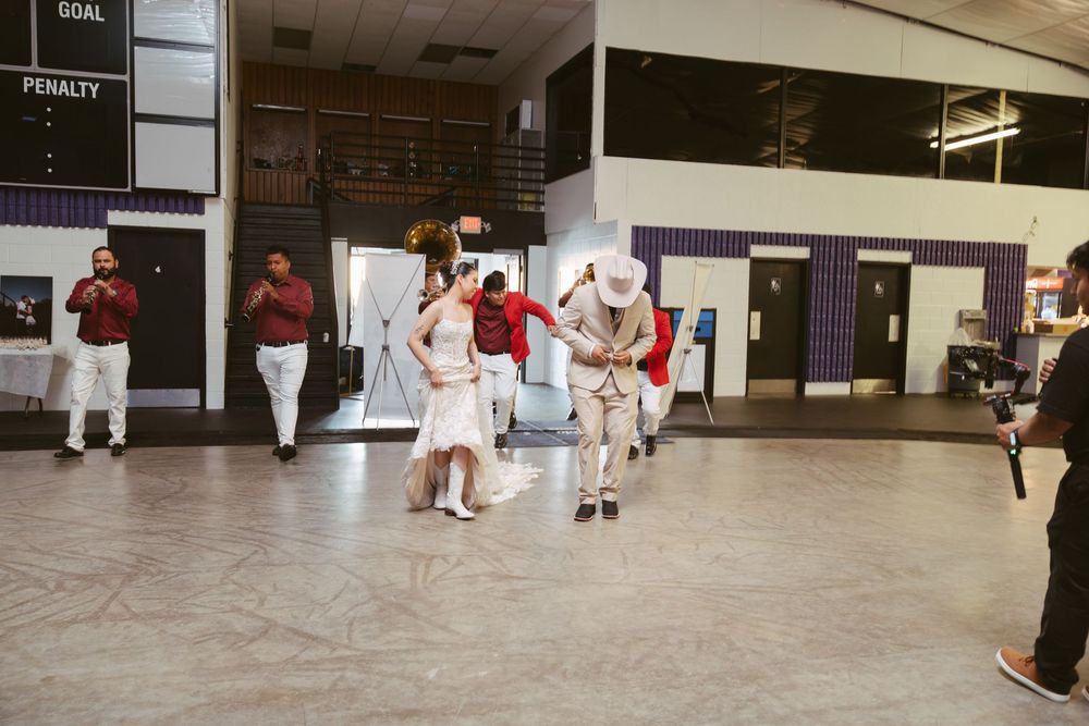 Couples dancing in traditional attire at an indoor cultural event with spectators watching in the background.