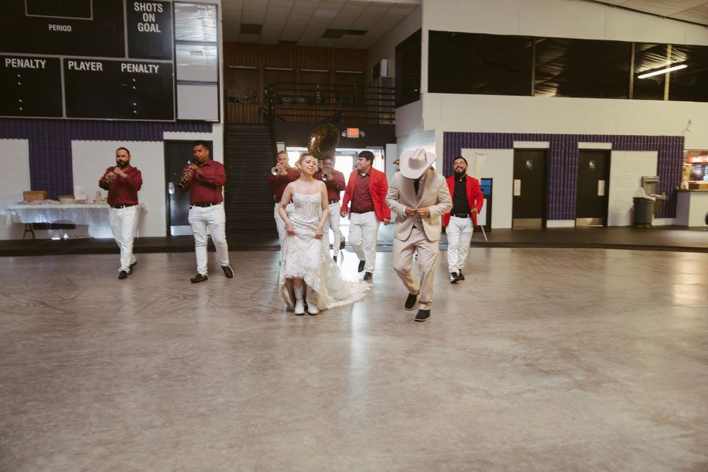 Group of people in costumes dancing and walking in a large indoor gymnasium or community center.