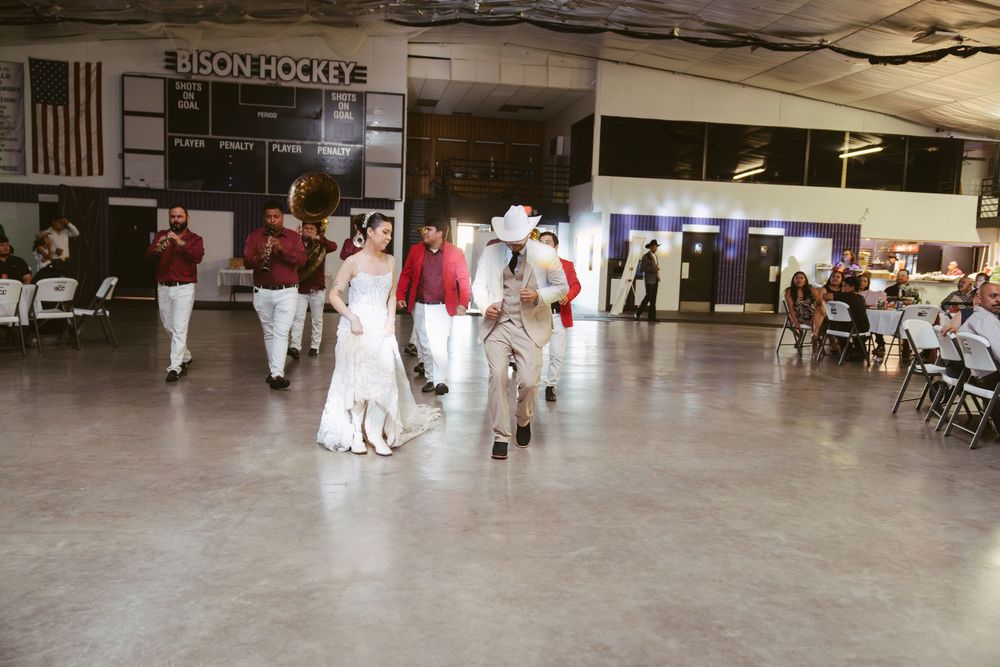 Wedding party processional in a Bison Hockey arena venue with guests seated at folding chairs.