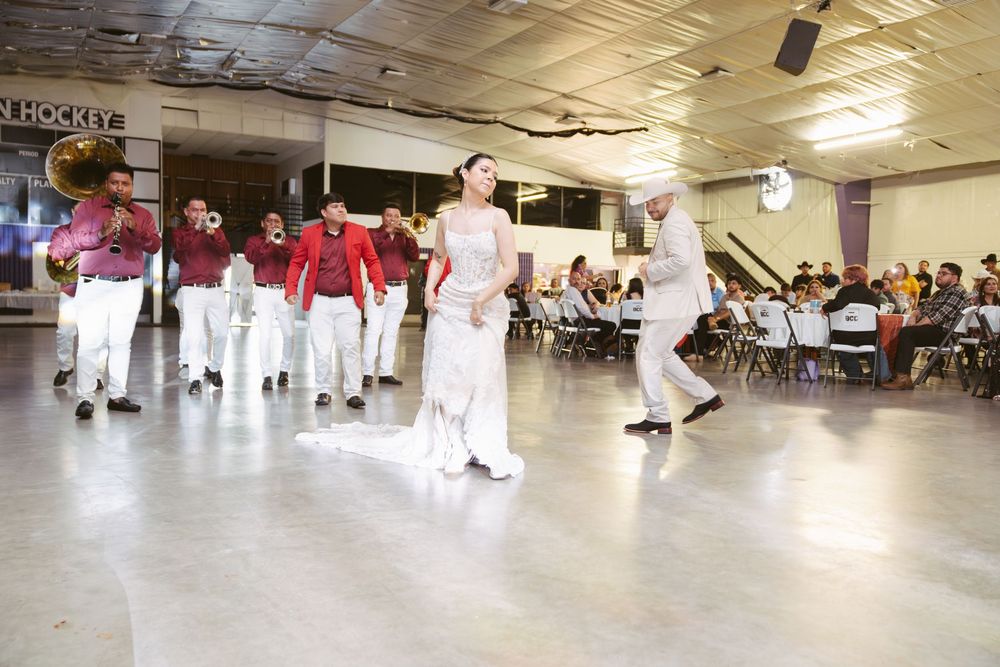 Mariachi band in red jackets performs with dancers in white at an indoor cultural event.