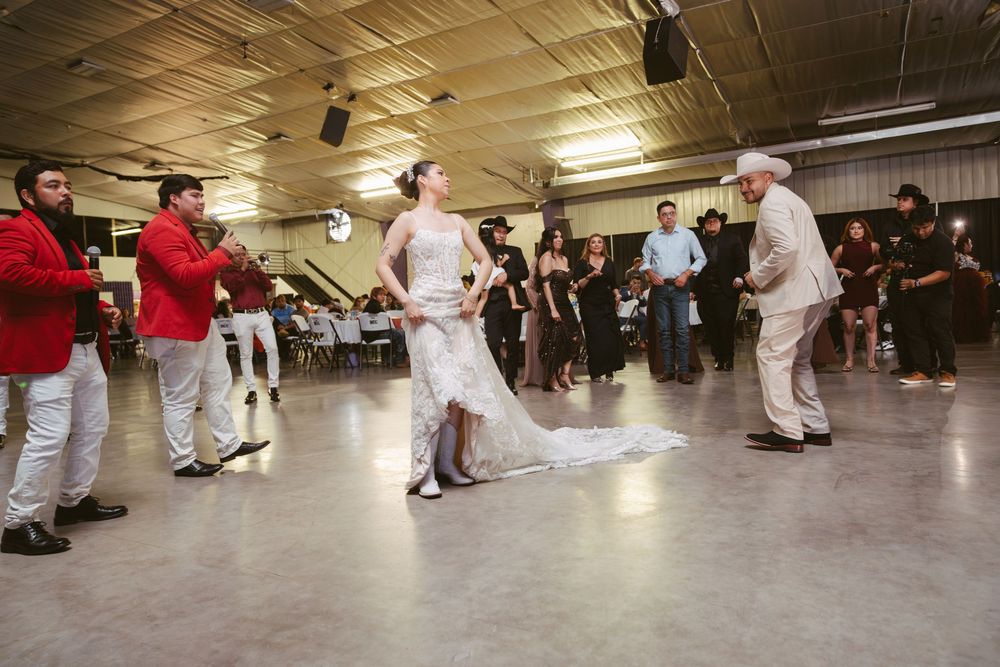 Bride dancing with elderly man at wedding reception while mariachi band performs in festive hall.