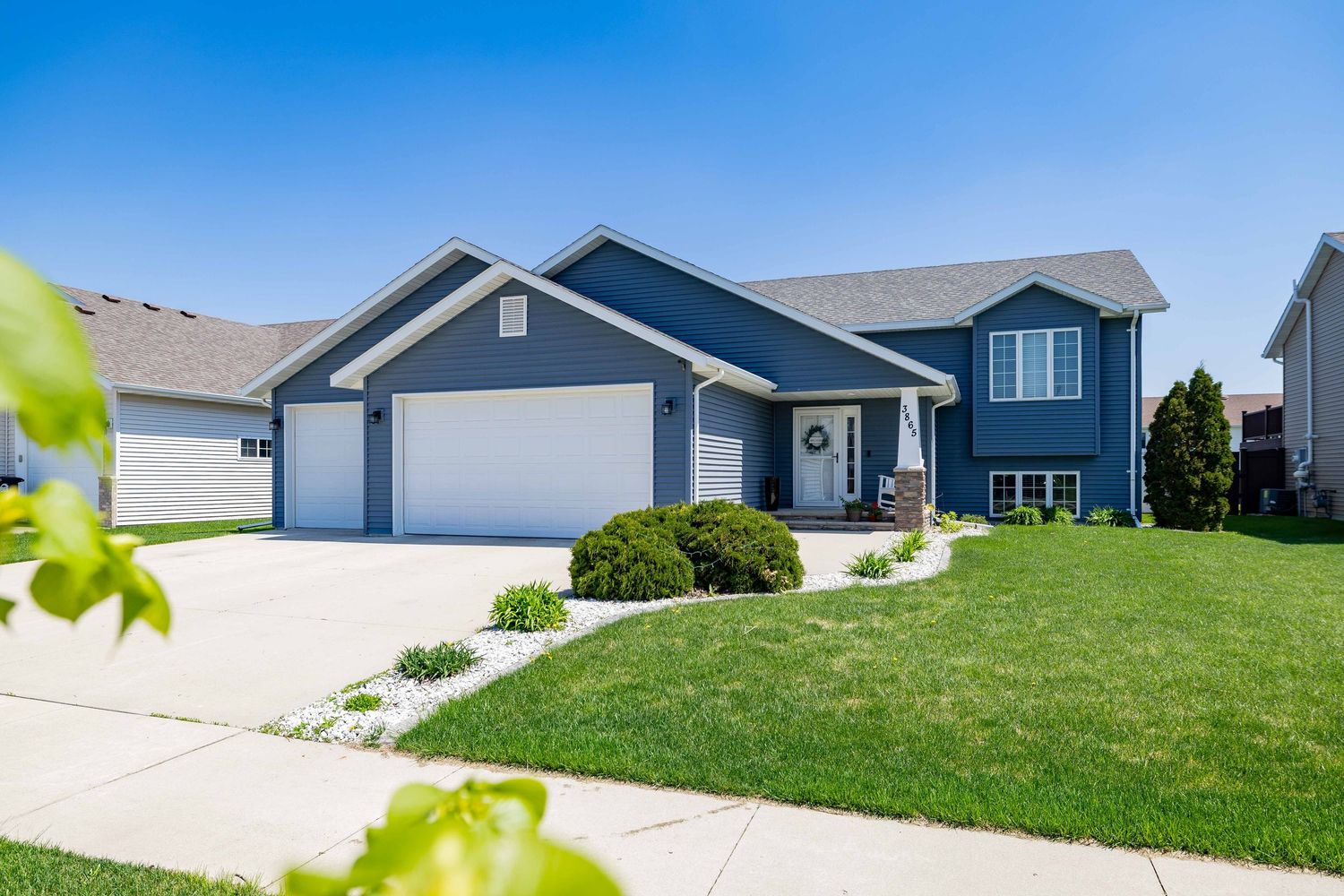 Blue two-car garage home with manicured lawn, concrete driveway, and landscaped shrubs under a clear blue sky.