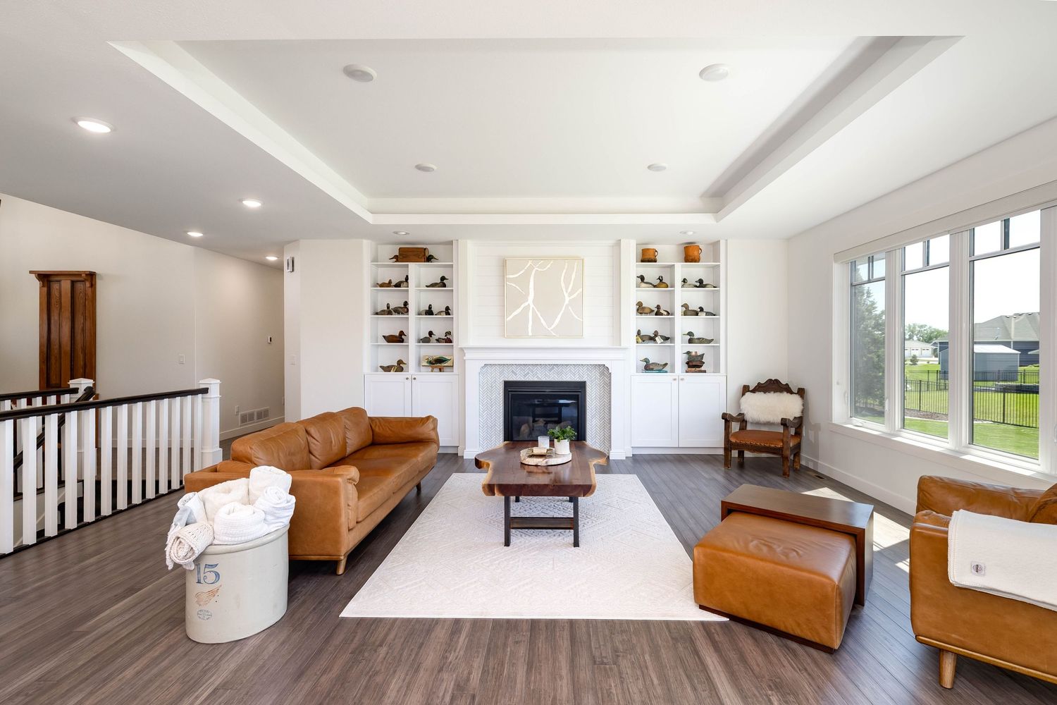 Elegant living room with tray ceiling, built-in shelves, white fireplace, tan leather sofas, and dark hardwood floors.