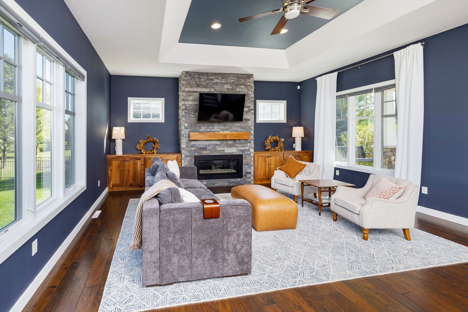 Elegant living room with navy blue walls, stone fireplace, hardwood floors, and stylish furniture on a light area rug.