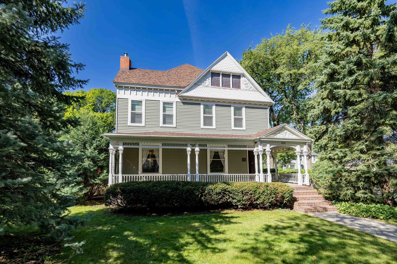 Victorian-style two-story home with wrap-around porch, gray siding, and mature trees.