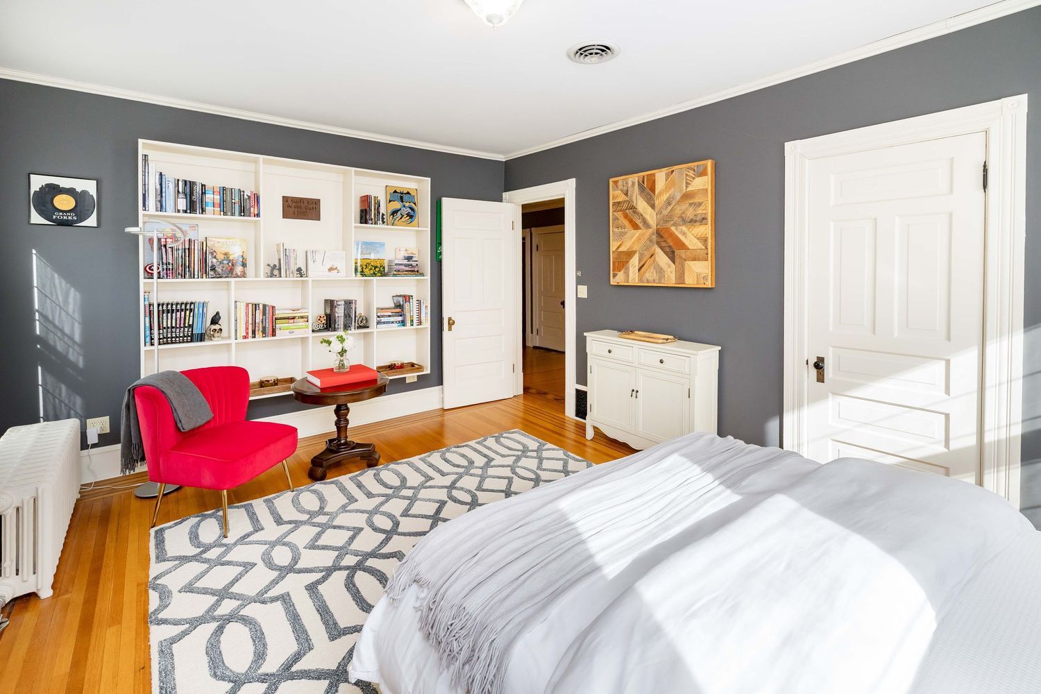Bright bedroom with built-in bookshelves, red chair, white dresser, and geometric area rug.