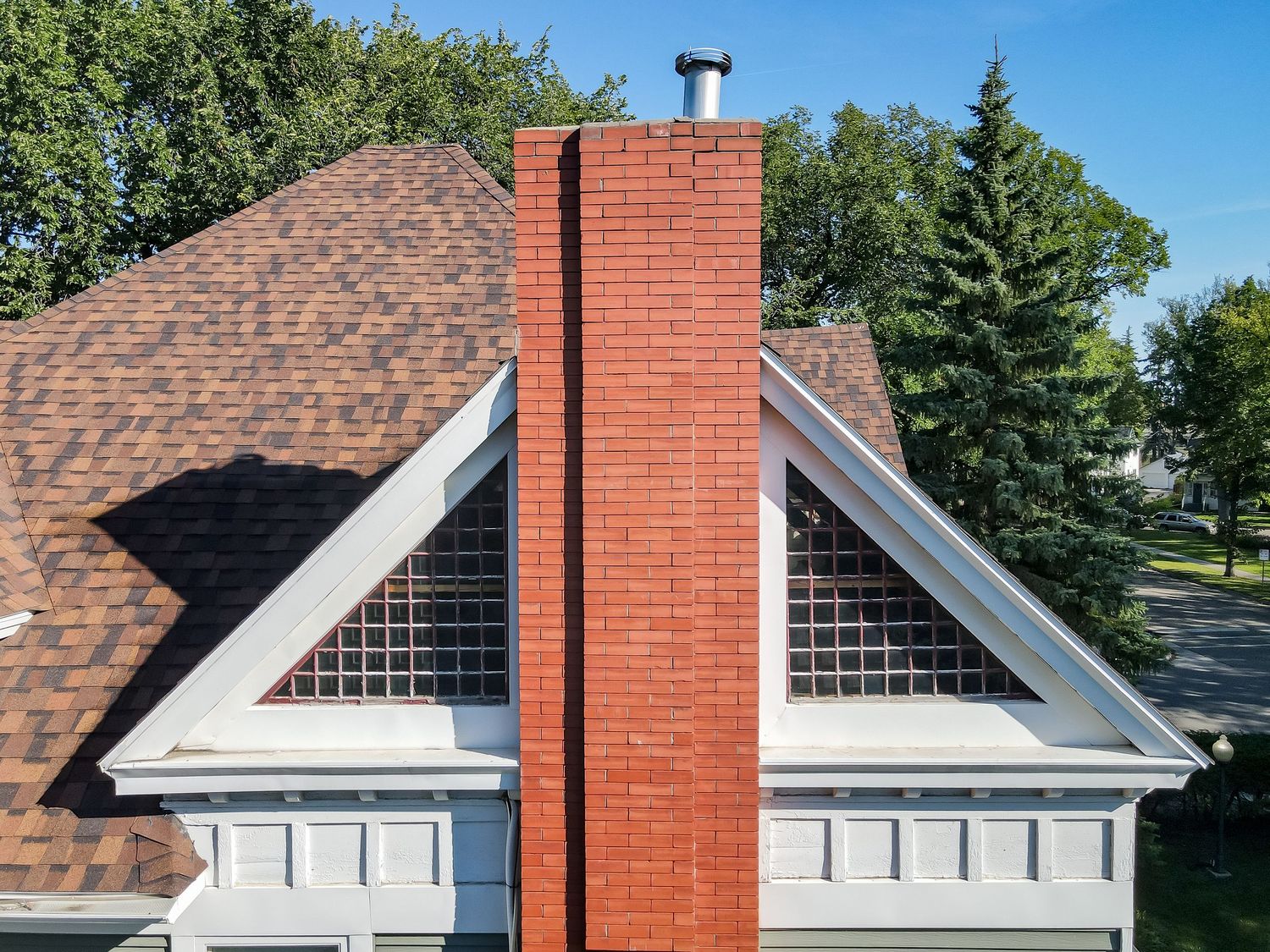 Aerial view of a brick chimney on a residential home with brown shingle roof and white gabled dormers.