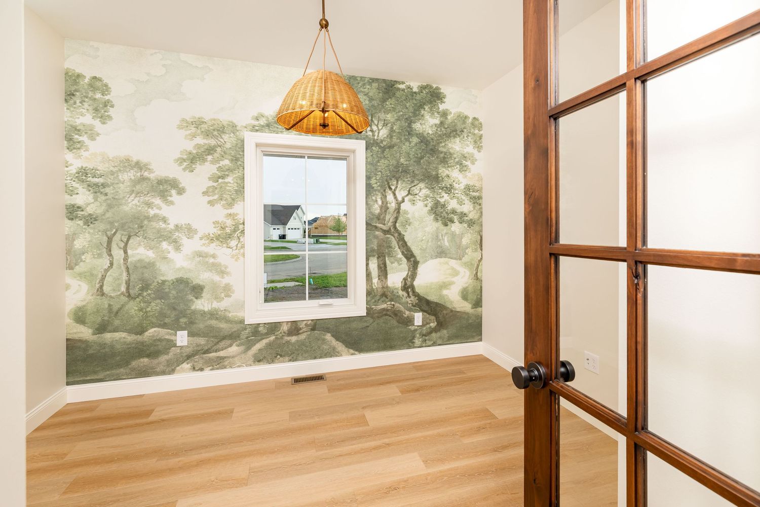 Room with scenic forest mural wallpaper, hardwood floors, a window, rattan pendant light, and a wood-framed glass door.