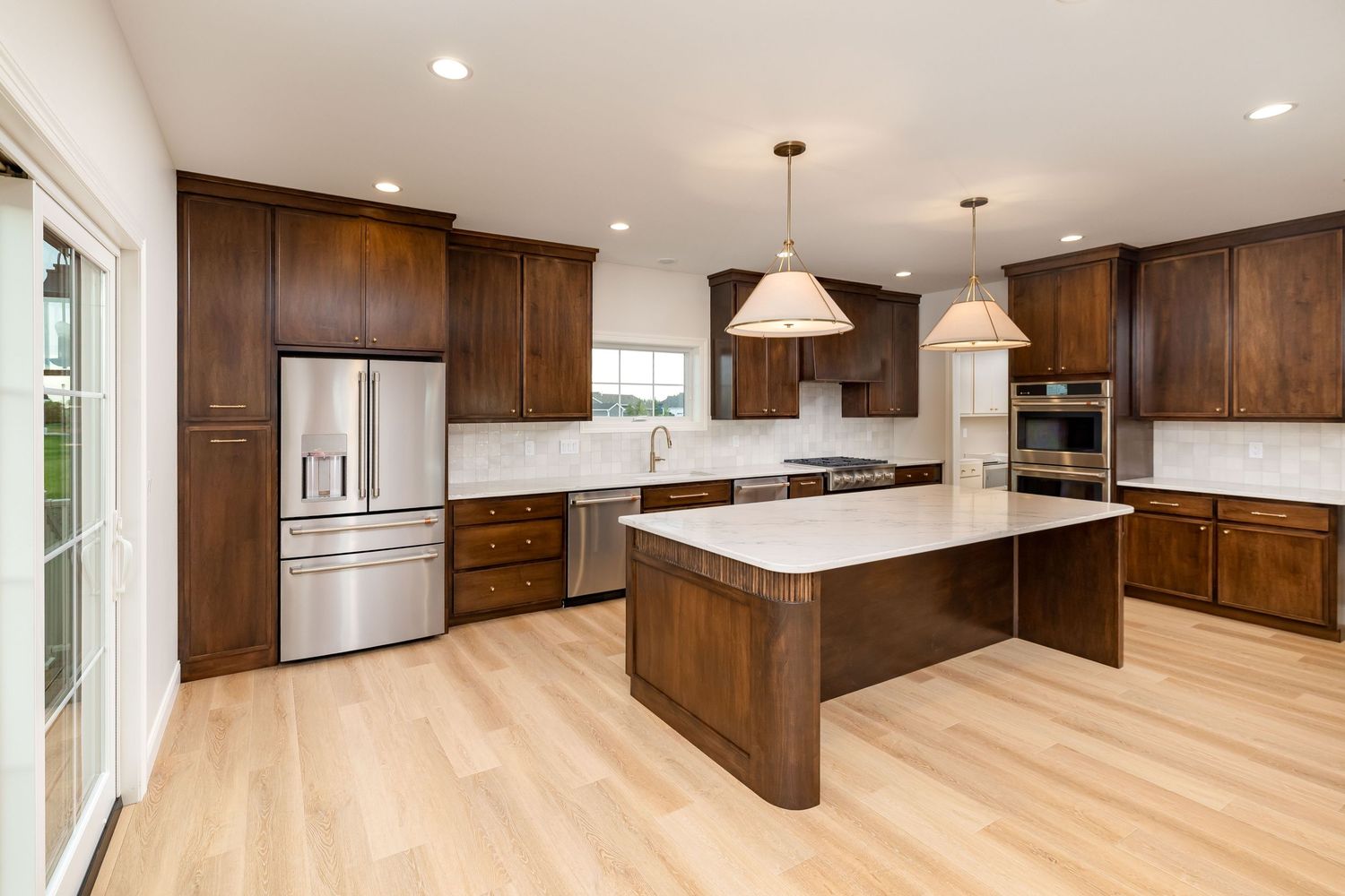 Modern kitchen with dark wood cabinets, stainless steel appliances, white quartz countertops, center island, and light hardwood floors.