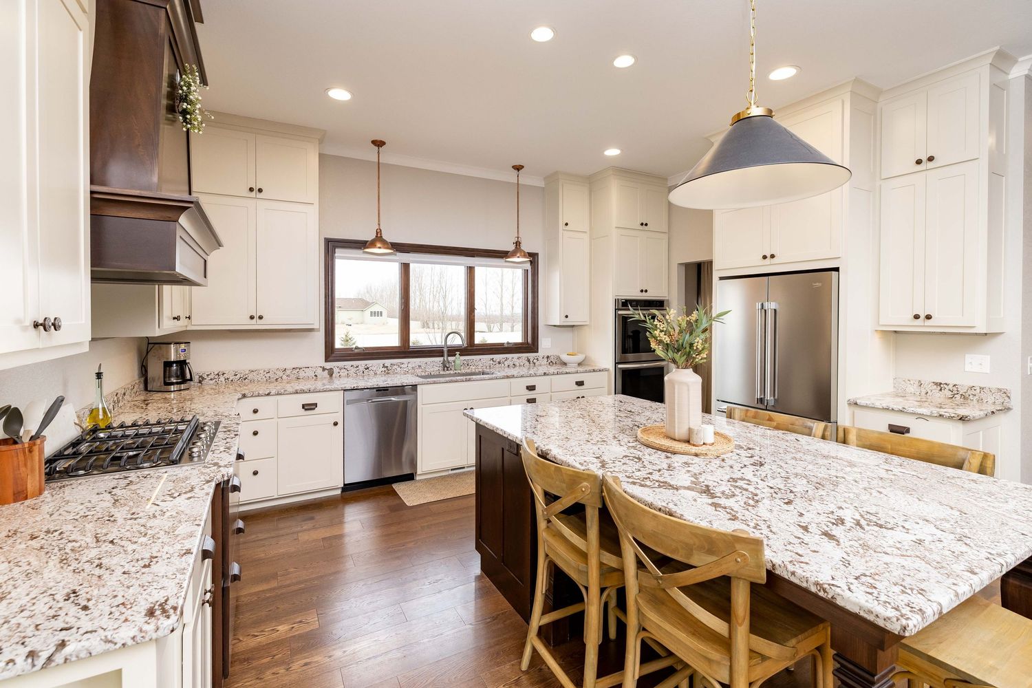 Spacious kitchen with white cabinets, granite island, pendant lights, stainless appliances, and hardwood floors.