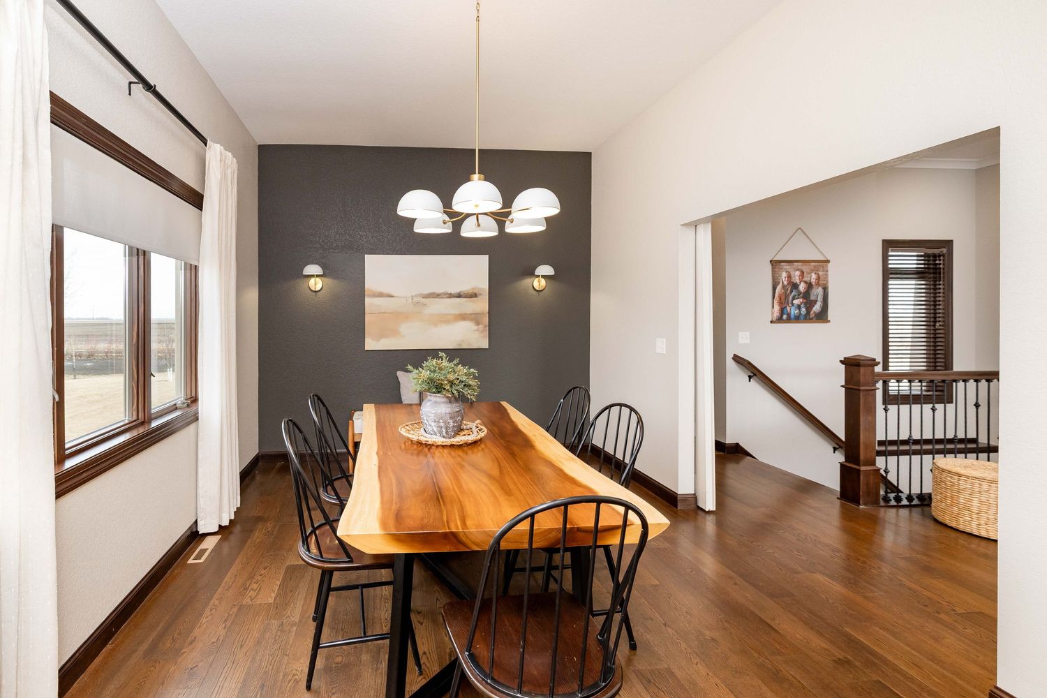 Dining room with live-edge wood table, black chairs, dark accent wall, hardwood floors, and elegant pendant lighting.