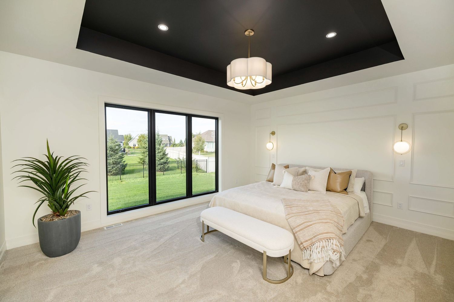 Elegant master bedroom with black tray ceiling, chandelier, wall sconces, neutral carpet, and sliding glass doors to backyard.