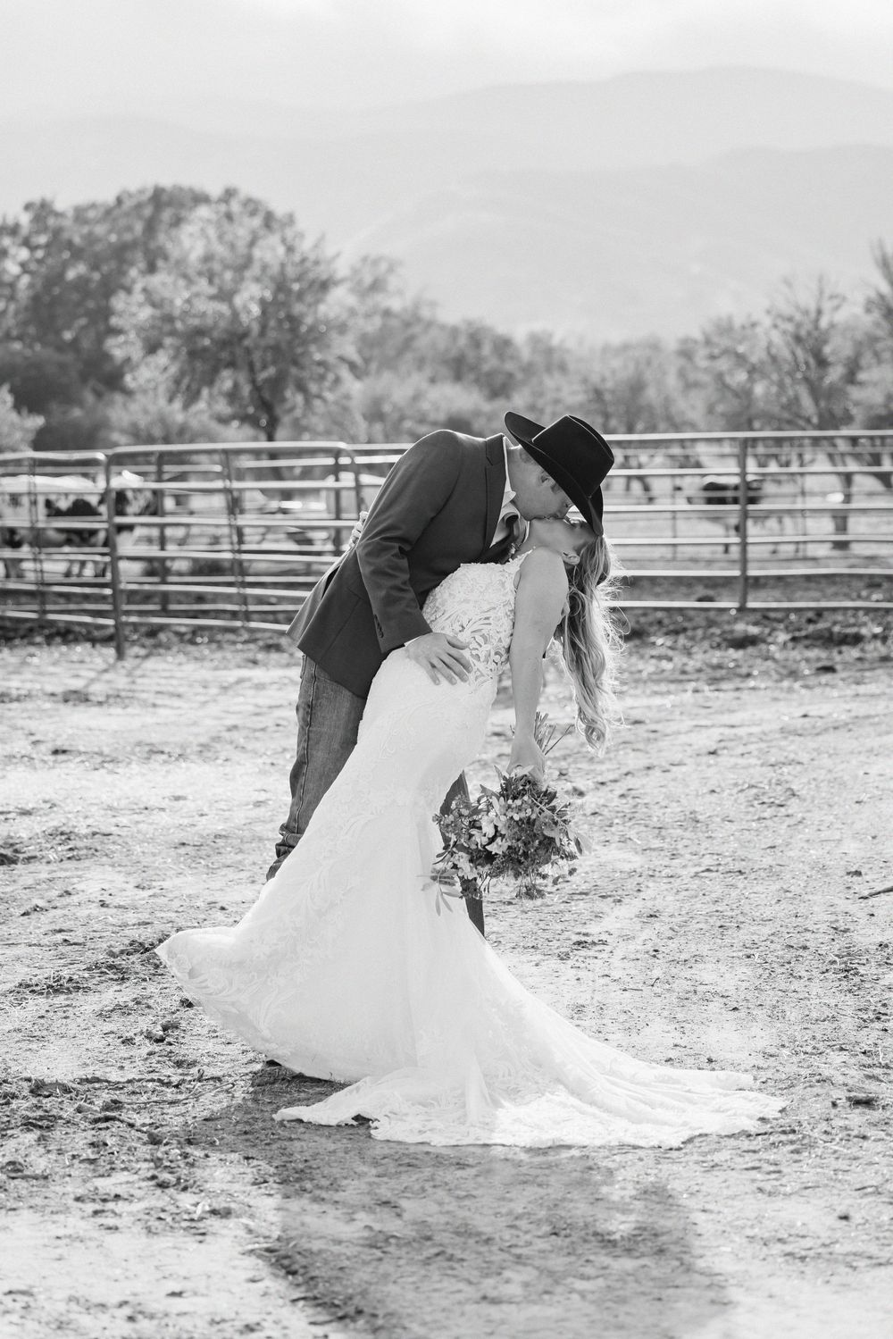 Black and white photo of a bride and groom sharing a romantic dip kiss at a rustic ranch wedding venue.