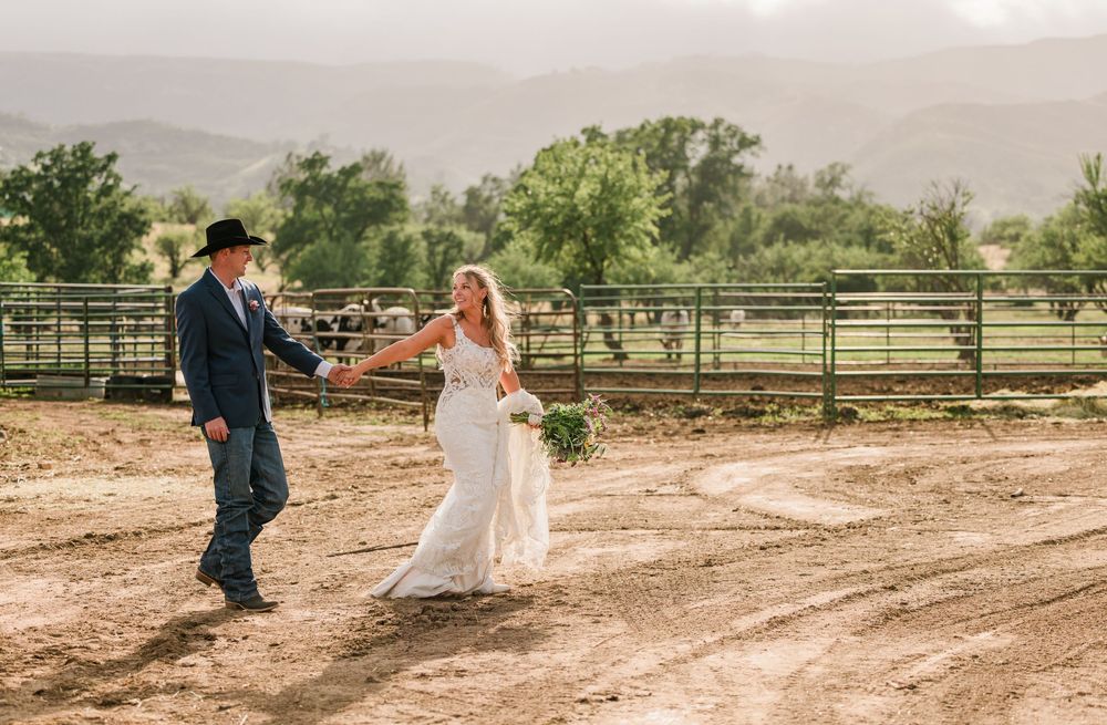 Bride and groom dancing on a rustic ranch with mountain views and cattle in the background.