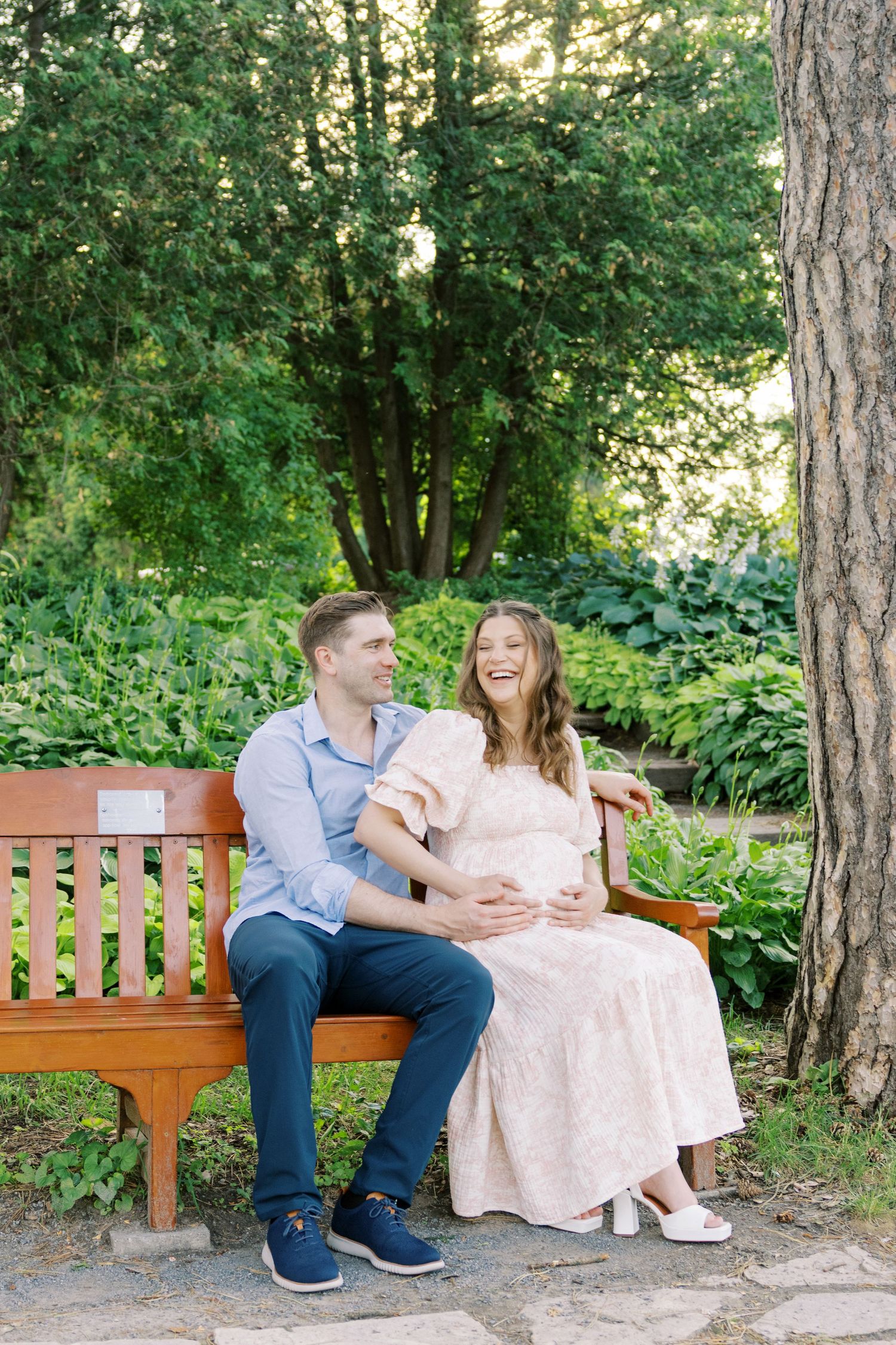 Smiling pregnant woman in pink floral dress holding ultrasound photo among red roses in garden.